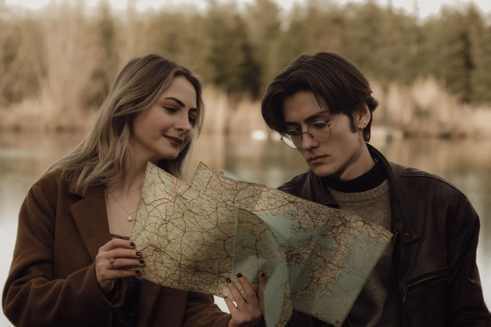 Pareja joven consultando un mapa junto a un lago mientras planifica su viaje de novios
