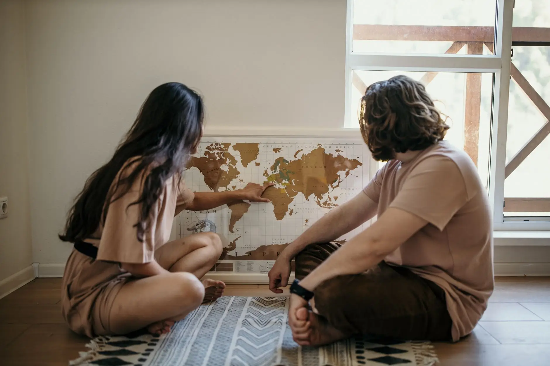 Pareja sentada en el suelo señalando destinos en un mapa del mundo mientras planifica su viaje de novios