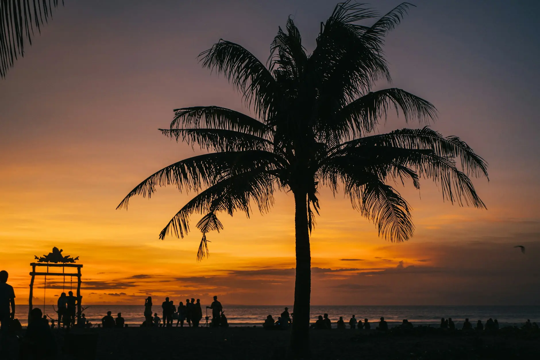 Silueta de una palmera y paseantes al atardecer en una playa del sur de Bali