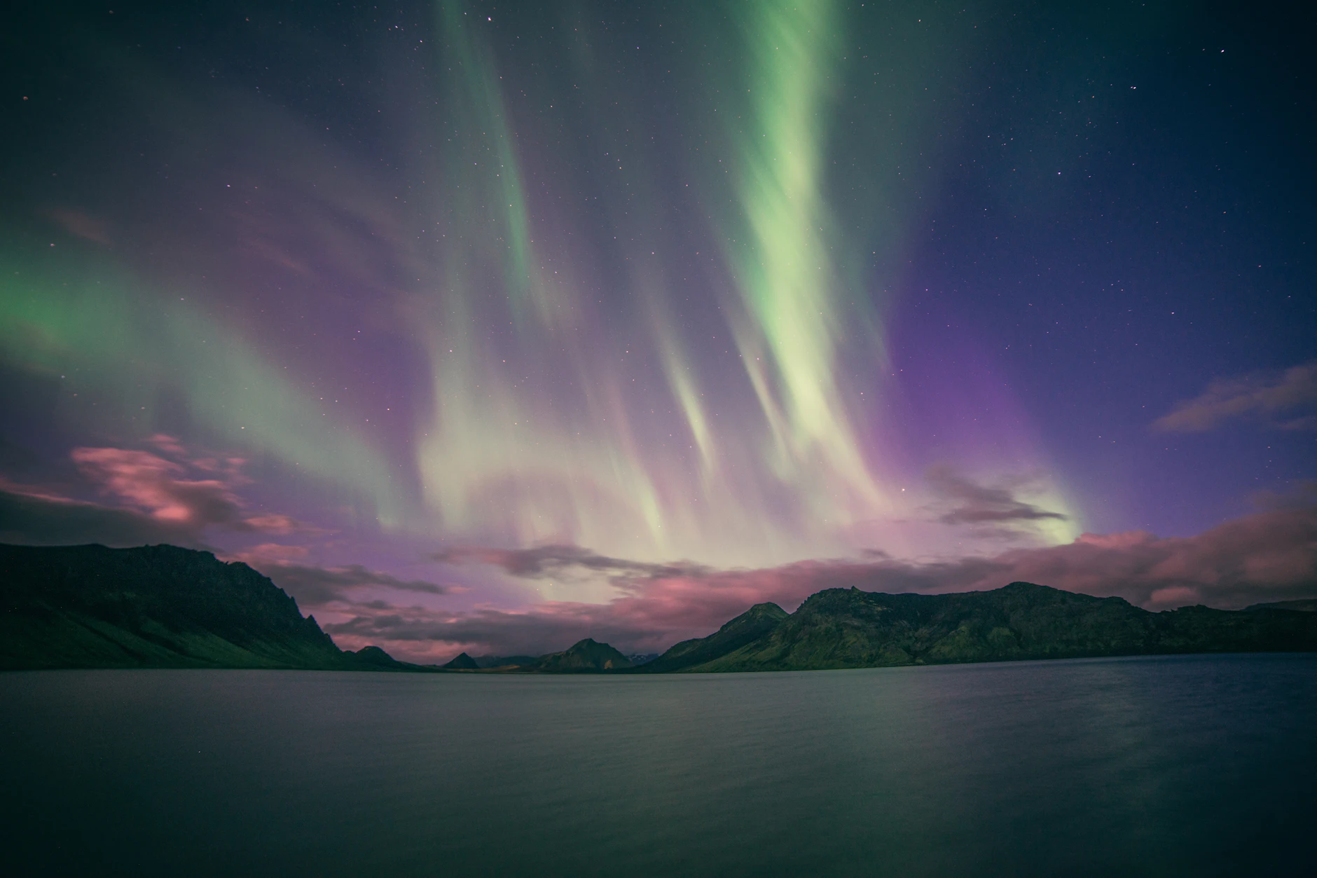 Aurora boreal verde y violeta danzando sobre un lago oscuro y montañas en Islandia