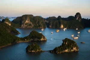 Barcos de crucero navegando entre los islotes kársticos de la bahía de Halong, Vietnam, al atardecer