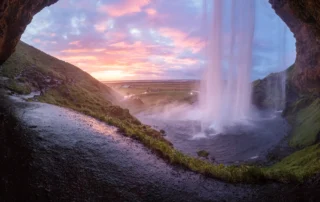 Cascada de Seljalandsfoss vista desde detrás al atardecer, Islandia Cascada de Seljalandsfoss vista desde la cueva de detrás con cielo rosado al atardecer en Islandia