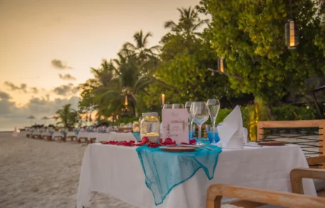 Cena romántica en la playa al atardecer en Maldivas Mesa para cena romántica con pétalos y farolillos sobre la arena al atardecer en Maldivas