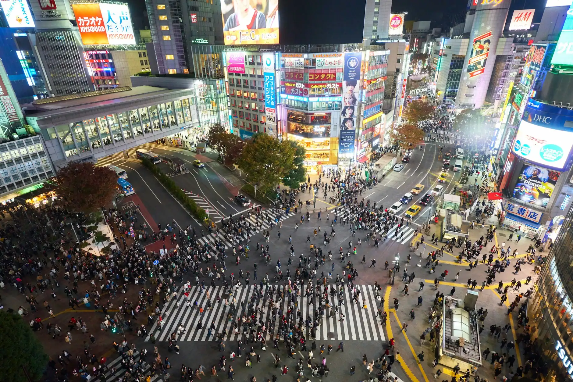 Multitud cruzando el famoso cruce de Shibuya en Tokio de noche, rodeado de pantallas y neones