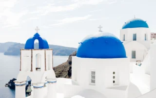 Cúpulas azules y campanario blanco de una iglesia de Santorini frente al mar Egeo