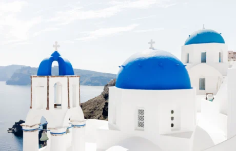 Cúpulas azules y campanario blanco de una iglesia de Santorini frente al mar Egeo