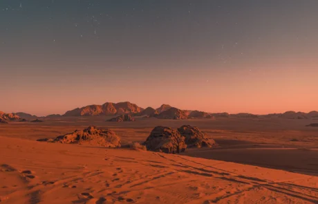 Wadi Rum basamortuko duna gorriak ilunabarrean izarrekin Wadi Rum basamortuko hare gorria eta mendiak ilunabarrean, lehen izarren azpian, Jordania