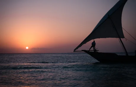 Dhow tradizional baten silueta, bela zabalik, ilunabarrean nabigatzen Zanzibar parean