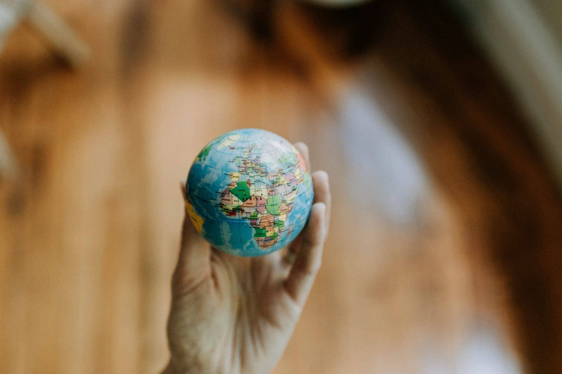 Mano sosteniendo un pequeño globo terráqueo sobre fondo cálido, como quien decide el destino del viaje de novios