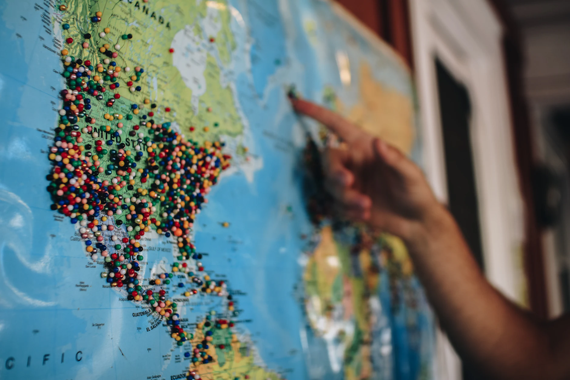 Mano señalando un destino en un mapa del mundo lleno de chinchetas de colores al planificar el viaje