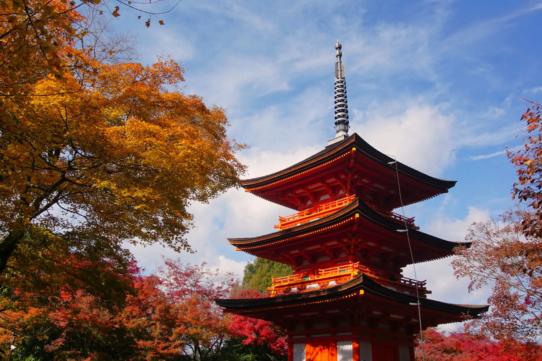 Pagoda bermellón de tres pisos en Kioto rodeada de arces rojos y dorados bajo el cielo azul de otoño