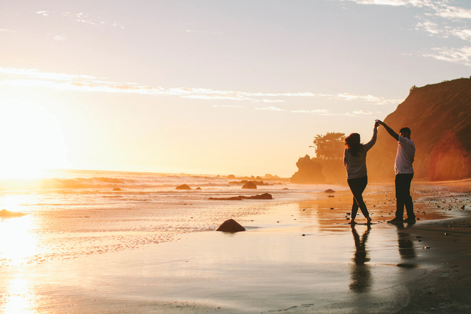Silueta de una pareja bailando cogida de la mano en la orilla de una playa al atardecer dorado