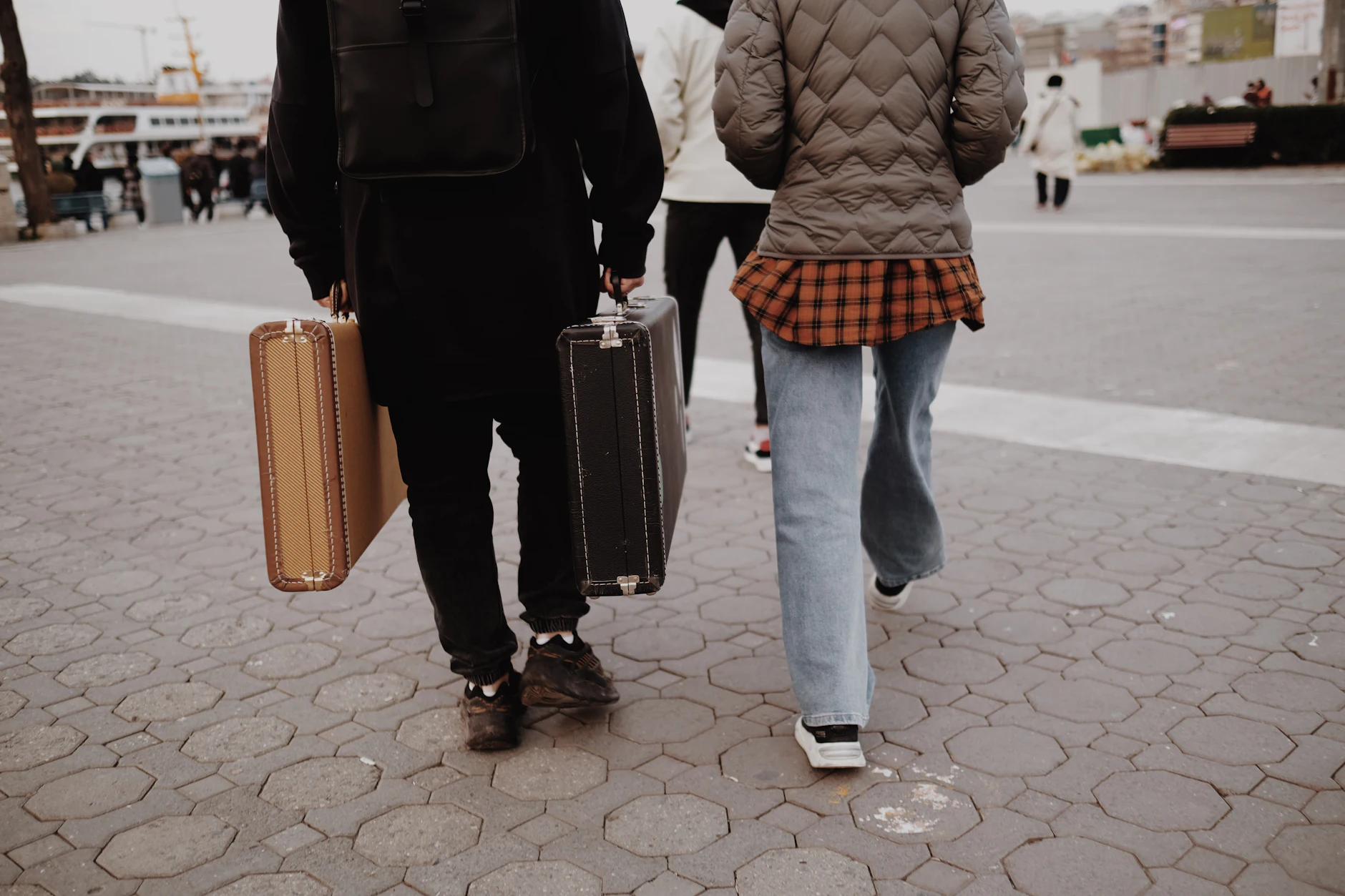 Pareja de espaldas caminando junto al puerto con dos maletas de estilo vintage al empezar su viaje