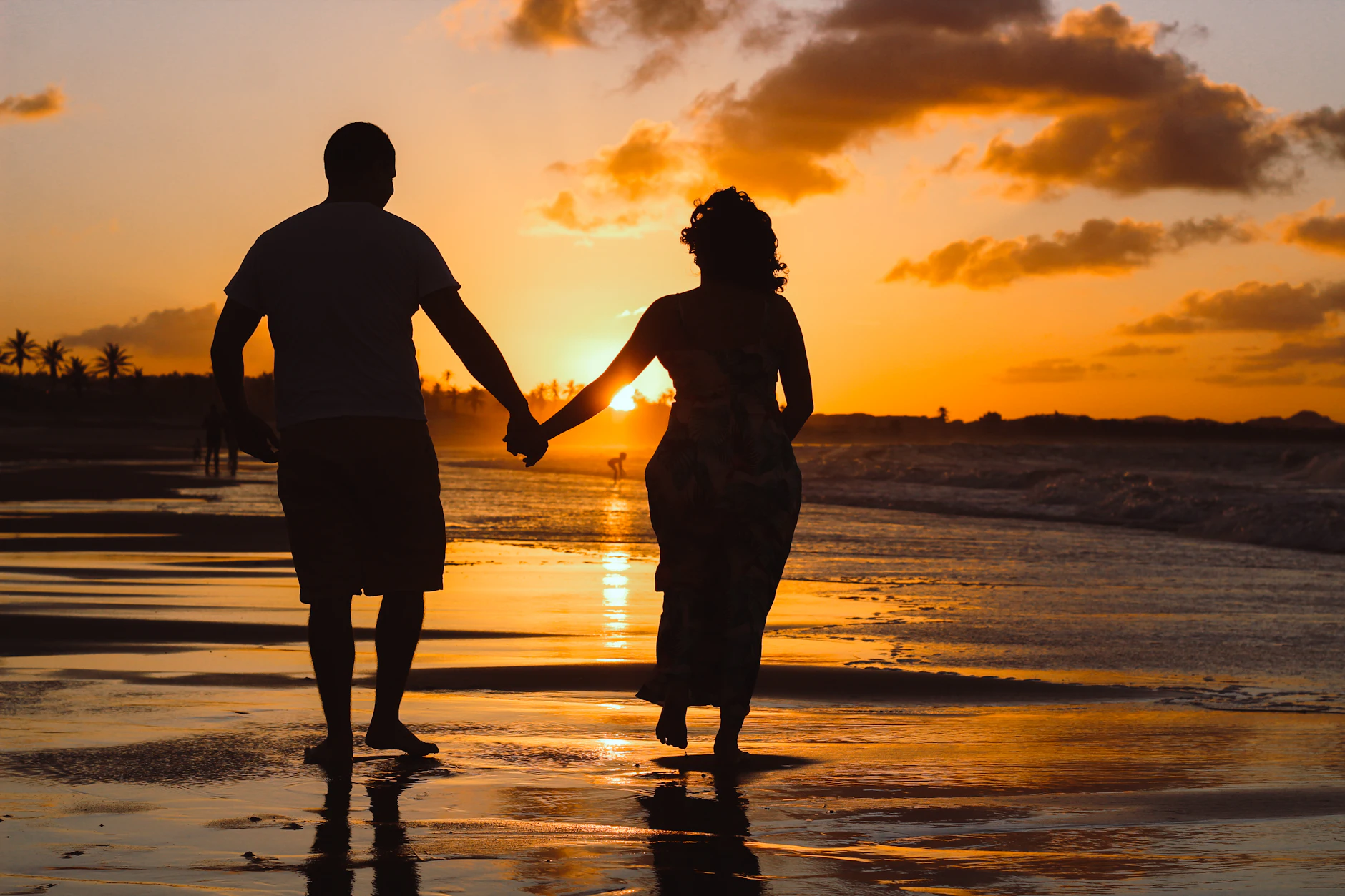 Silueta de una pareja de recién casados paseando de la mano por la orilla al atardecer