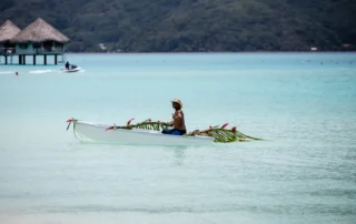 Piragua polinesia decorada navegando por la laguna turquesa de Bora Bora Polinesio remando en una piragua adornada con hojas de palma en la laguna turquesa de Bora Bora