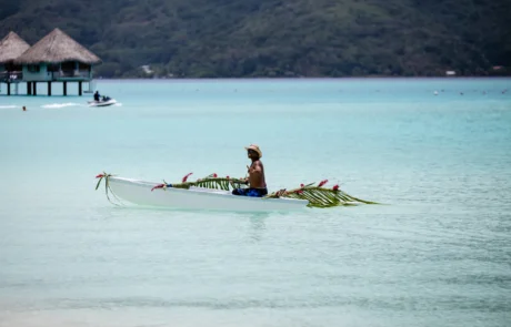 Piragua polinesia decorada navegando por la laguna turquesa de Bora Bora Polinesio remando en una piragua adornada con hojas de palma en la laguna turquesa de Bora Bora