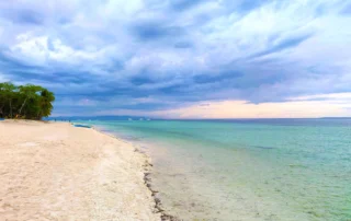 Playa de arena blanca con agua turquesa y cielo de nubes al atardecer en Bohol, Filipinas
