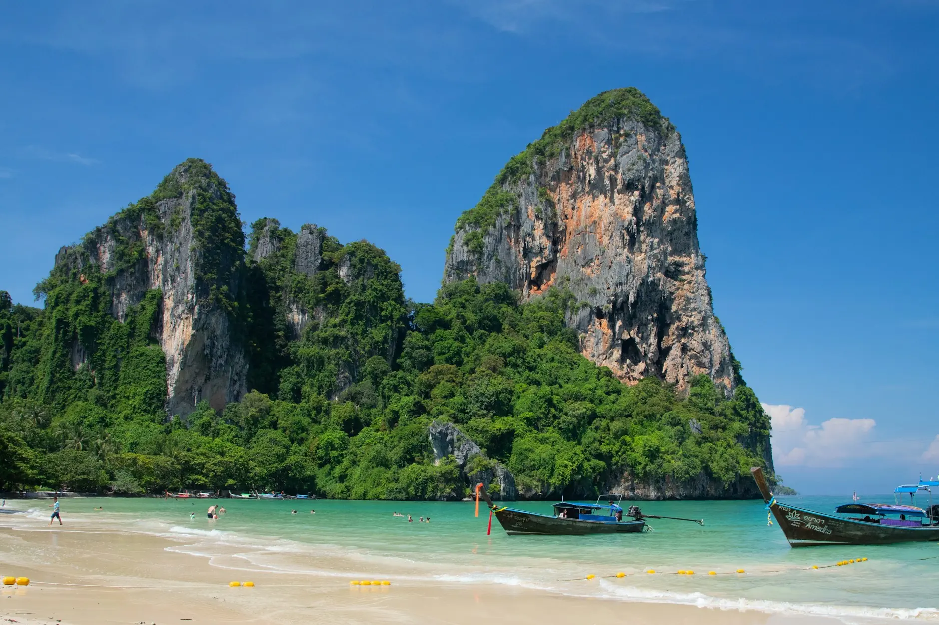 Barcas de cola larga en el agua turquesa de la playa de Railay, Krabi, bajo acantilados de roca caliza