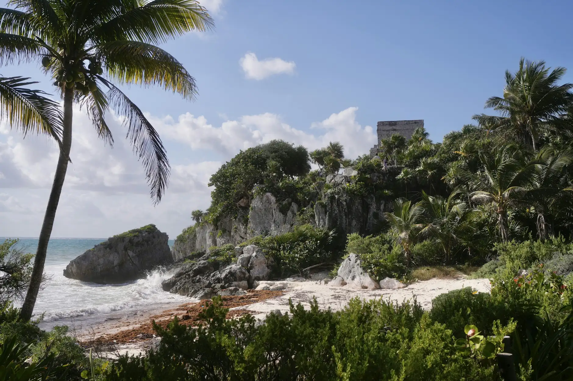 Templo maya de Tulum en lo alto del acantilado entre palmeras, junto a la playa del Caribe
