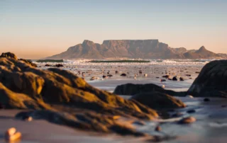 Table Mountain eta Lurmutur Hiria Bloubergstrand hondartzako harkaitzetatik ikusita, ilunabarrean