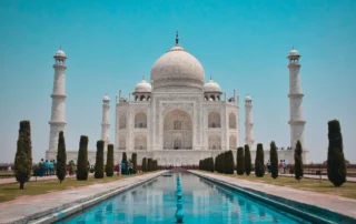 Taj Mahal de Agra con sus jardines y estanque central El Taj Mahal de Agra bajo un cielo azul despejado, con el estanque y los cipreses de sus jardines