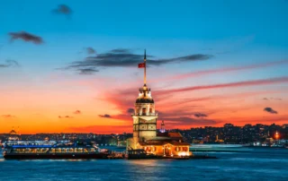 La Torre de la Doncella iluminada en el Bósforo bajo un cielo naranja de atardecer en Estambul