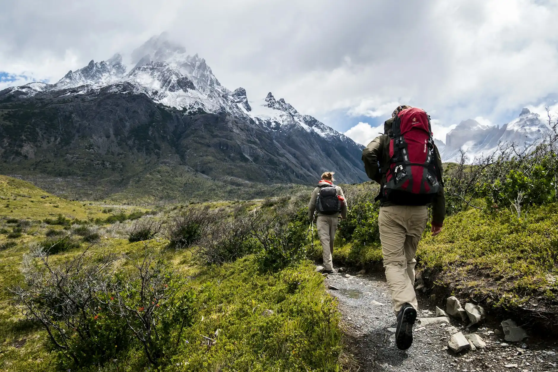 Dos excursionistas con mochila caminan por un sendero hacia las montañas nevadas de Torres del Paine, en la Patagonia