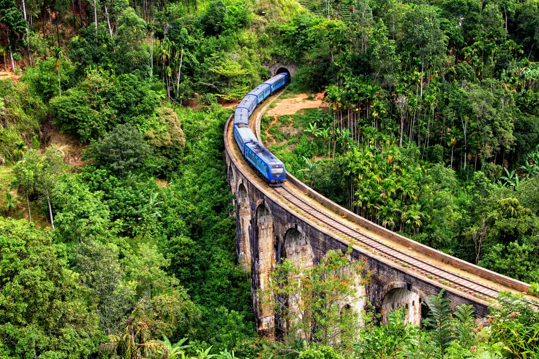 Tren azul cruzando el puente de los Nueve Arcos entre la selva verde de Ella, Sri Lanka
