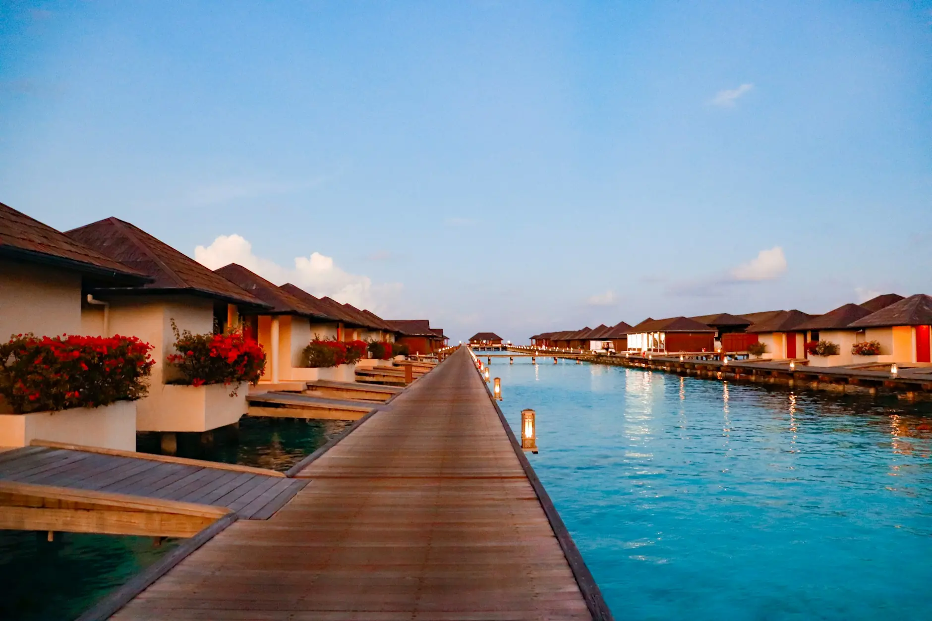 Villas sobre el agua en Maldivas con la primera luz Pasarela de madera entre villas sobre el agua y laguna turquesa al amanecer en Maldivas