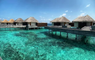 Villas con techo de paja sobre un arrecife de aguas cristalinas en un resort de Maldivas