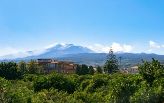 Volcán Etna nevado sobre la campiña verde de Sicilia El volcán Etna con la cumbre nevada asomando sobre campos y arboledas de Sicilia