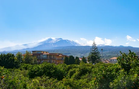 Volcán Etna nevado sobre la campiña verde de Sicilia El volcán Etna con la cumbre nevada asomando sobre campos y arboledas de Sicilia