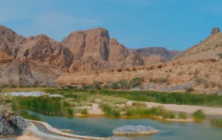 Ur turkesako putzuak eta landaredia mendi gorrixkaz inguratutako wadi batean, Omanen