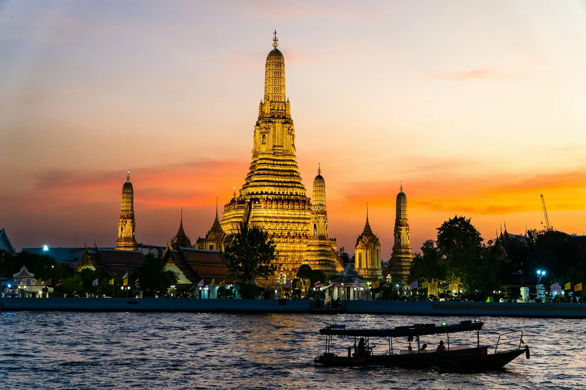 El templo Wat Arun iluminado al atardecer con barcas en el río Chao Phraya de Bangkok